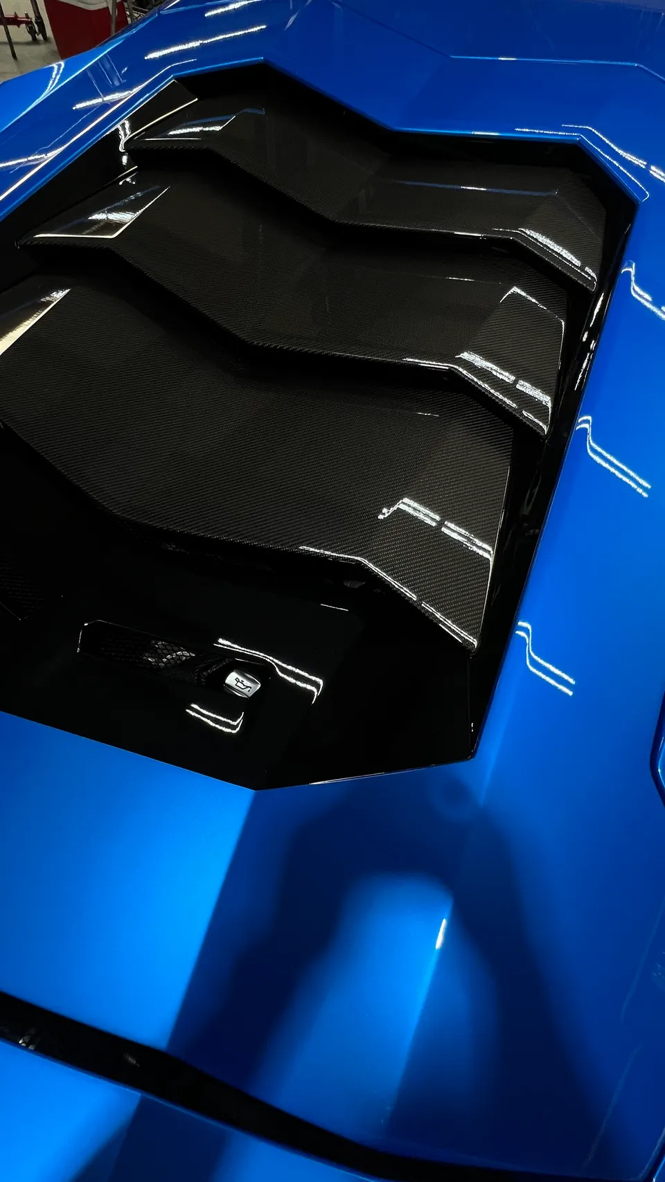 Blue Lamborghini engine cover with carbon fiber louvers and glossy paint finish