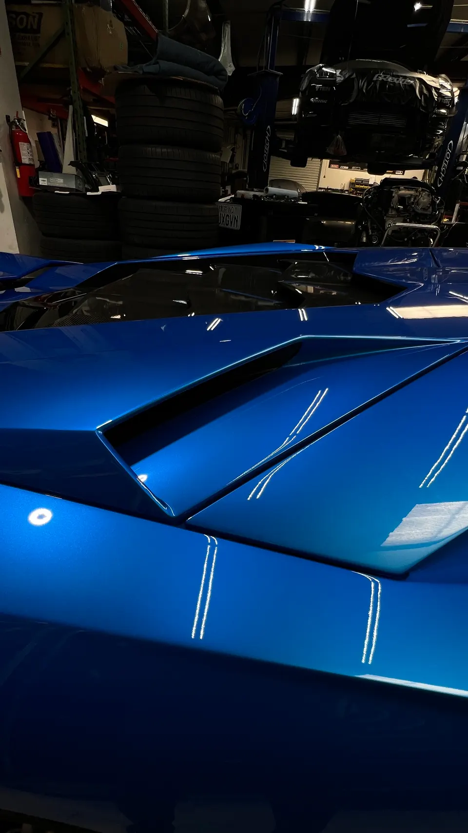Rear deck and engine cover of a blue supercar, likely a Lamborghini, in a performance tuning shop.