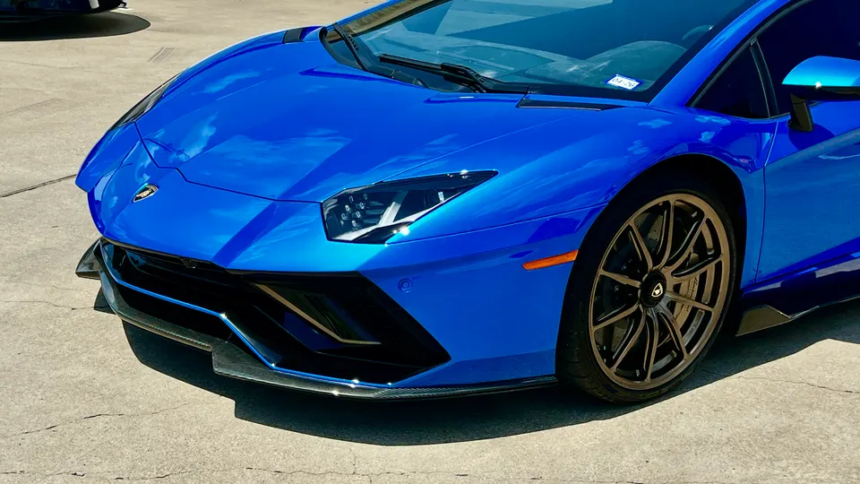 Blue Lamborghini Aventador with a carbon fiber front splitter parked on concrete.