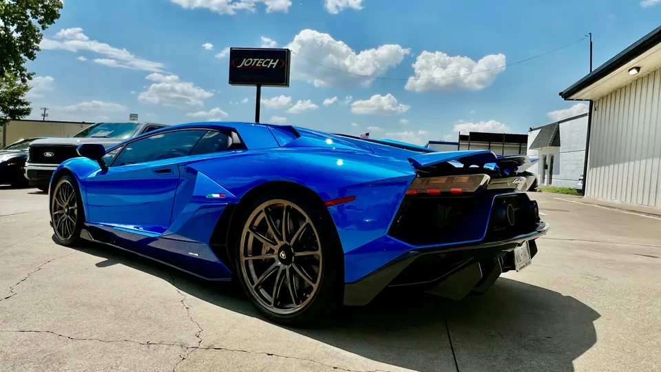 A blue Lamborghini Aventador parked outside Jotech Motorsports, showcasing its sleek design and rear diffuser.