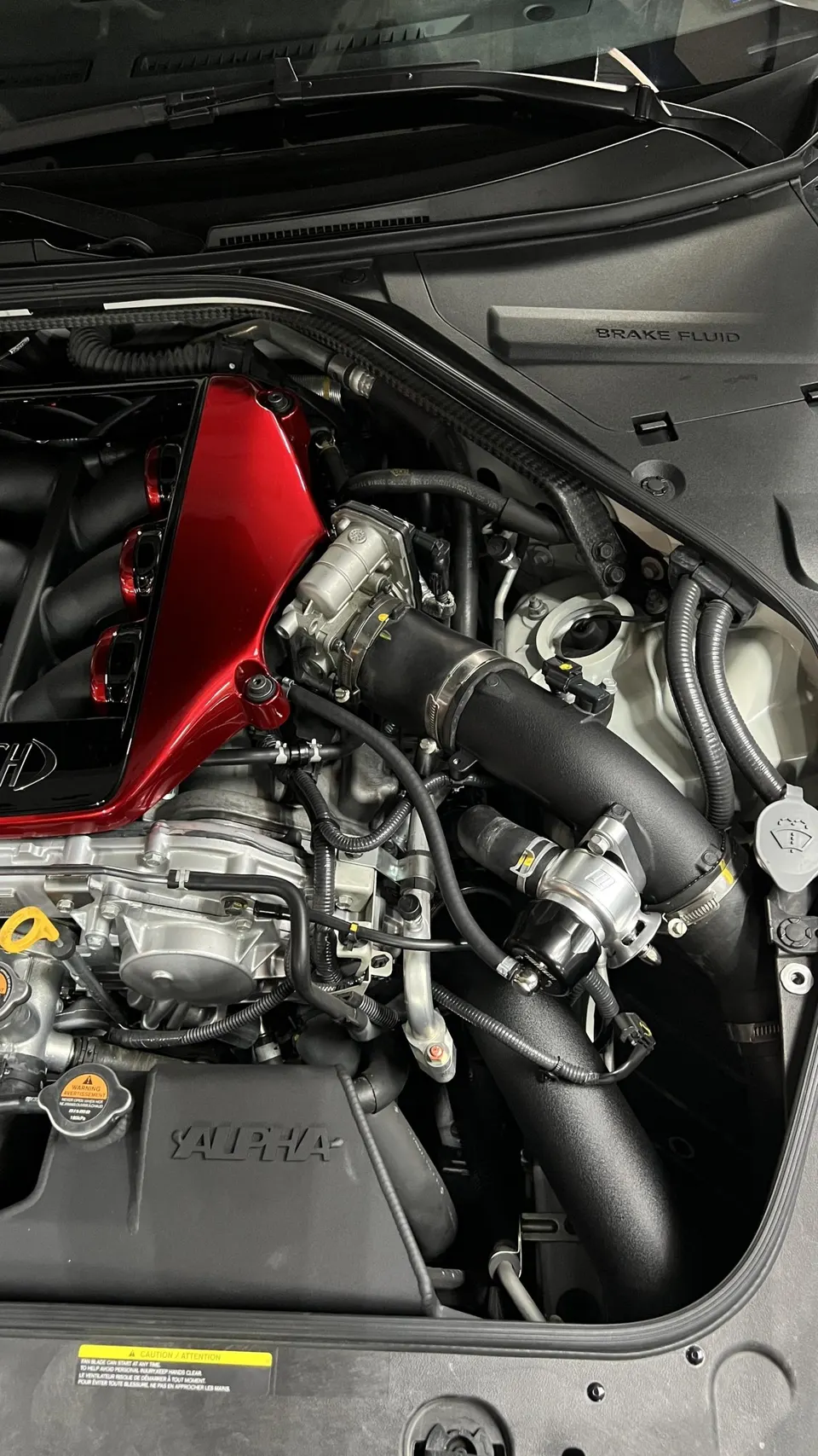 Close-up of a Nissan GT-R engine bay featuring an Alpha Performance aftermarket intake system and red engine cover.