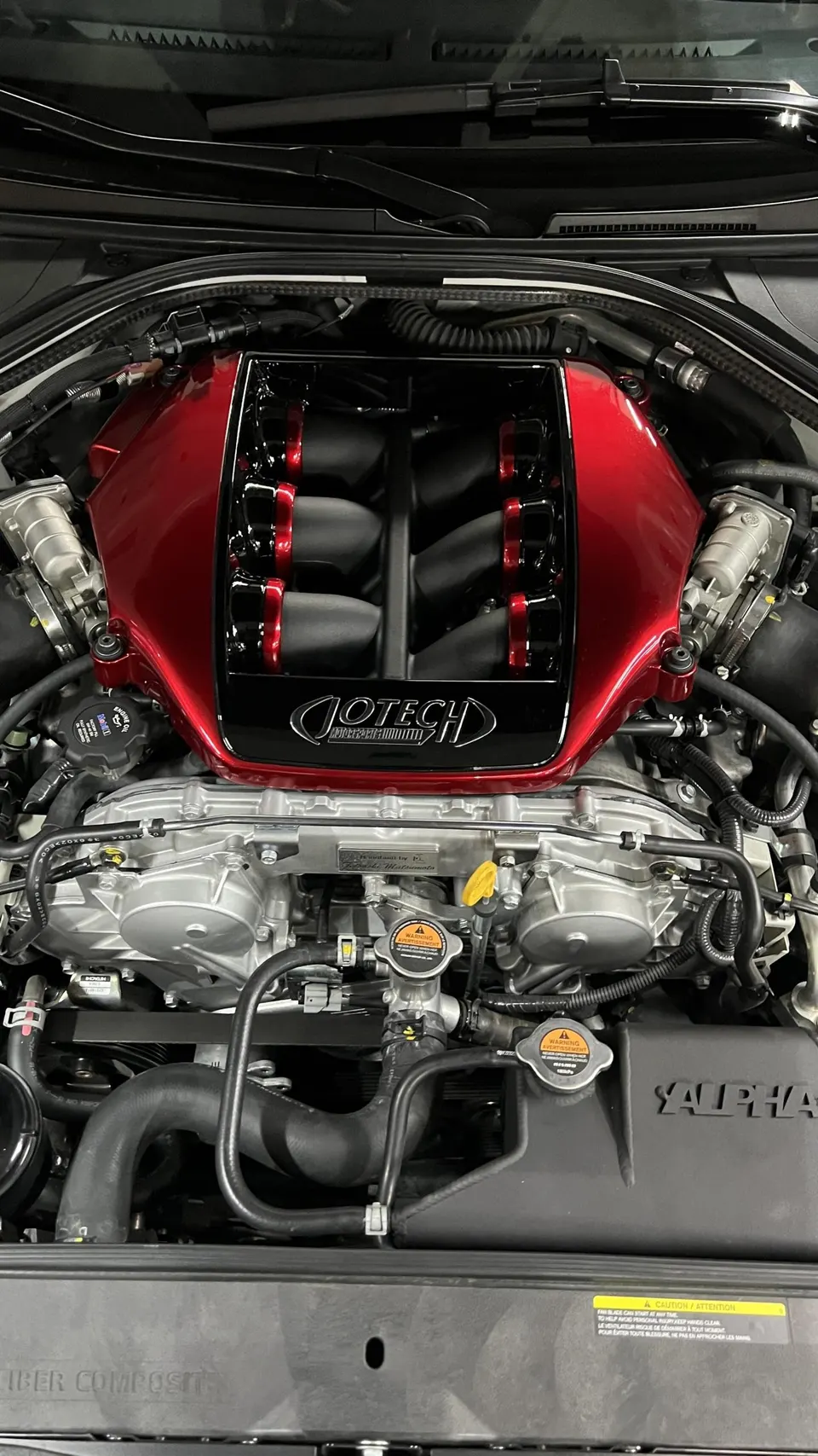 A detailed view of a Jotech tuned engine bay with a red intake manifold, showcasing performance components.