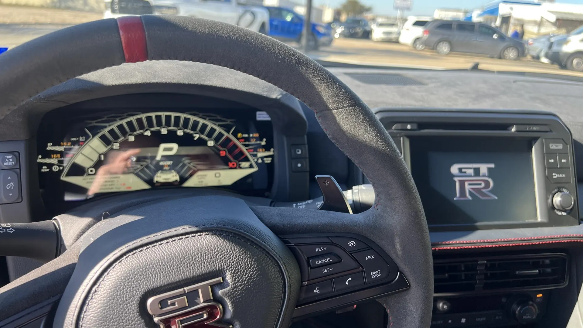 Interior view of a Nissan GT-R showing the alcantara steering wheel, digital dashboard, and infotainment screen with the GT-R logo.