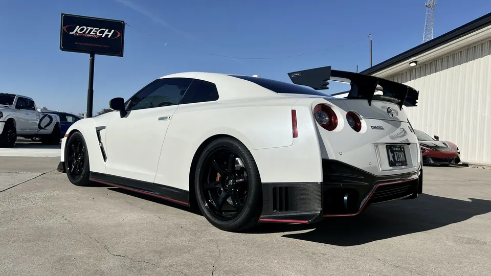White Nissan GT-R R35 with a large carbon fiber rear wing and aftermarket wheels parked outside Jotech Motorsports.