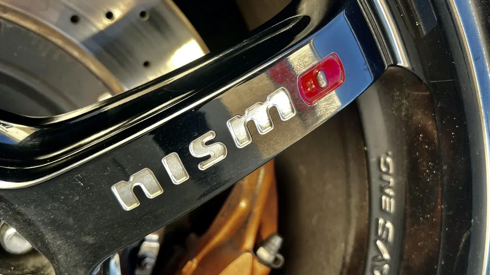 Close-up of a Nismo wheel with a bronze brake caliper and drilled rotor on a performance car.