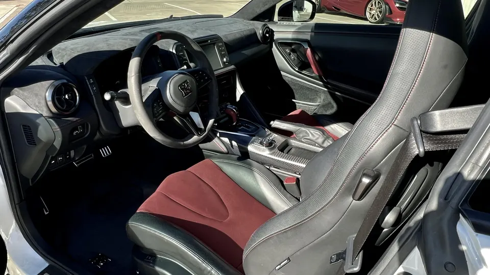 Interior view of a Nissan GT-R with red and black seats, carbon fiber trim, and a suede steering wheel.