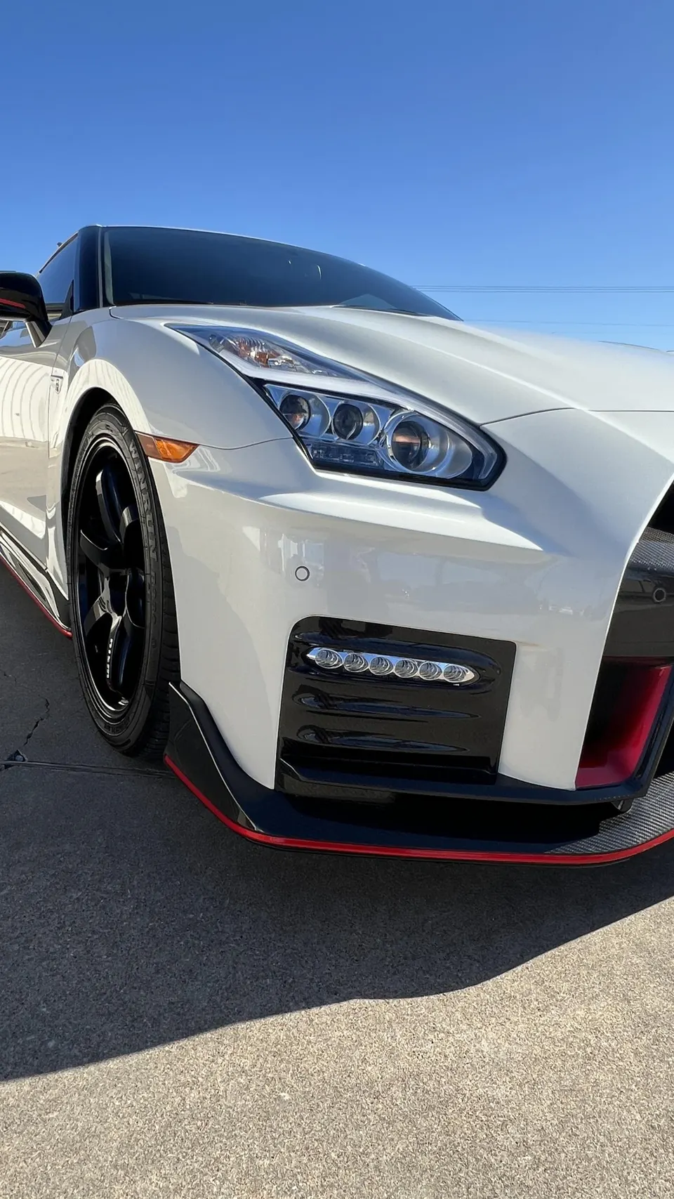 A white Nissan GT-R with a black front splitter and red accent line, showcasing its aggressive front design.