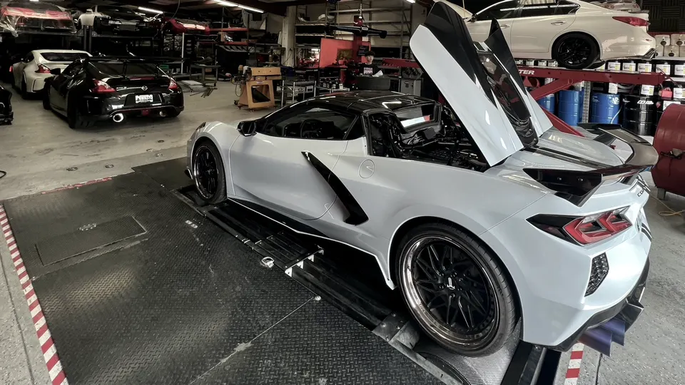 White Corvette C8 on a dyno in a performance tuning shop with its engine bay open, ready for testing.