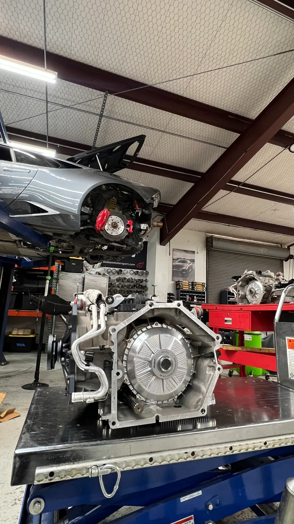 A Lamborghini Huracan on a lift in a performance shop with its transmission removed and on a workbench.