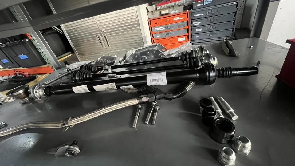 New driveshafts, braided lines, and various fittings laid out on a workbench in a performance tuning shop.