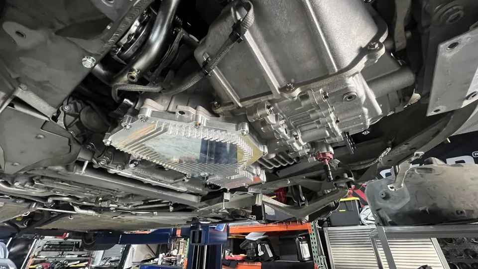 Underside view of a performance car on a lift, showcasing the transmission and an aftermarket pan.