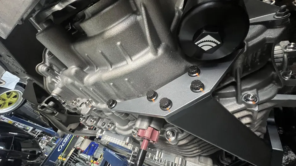 Close-up view of a car's underside, showing the engine oil pan, oil filter, and a silver chassis brace.