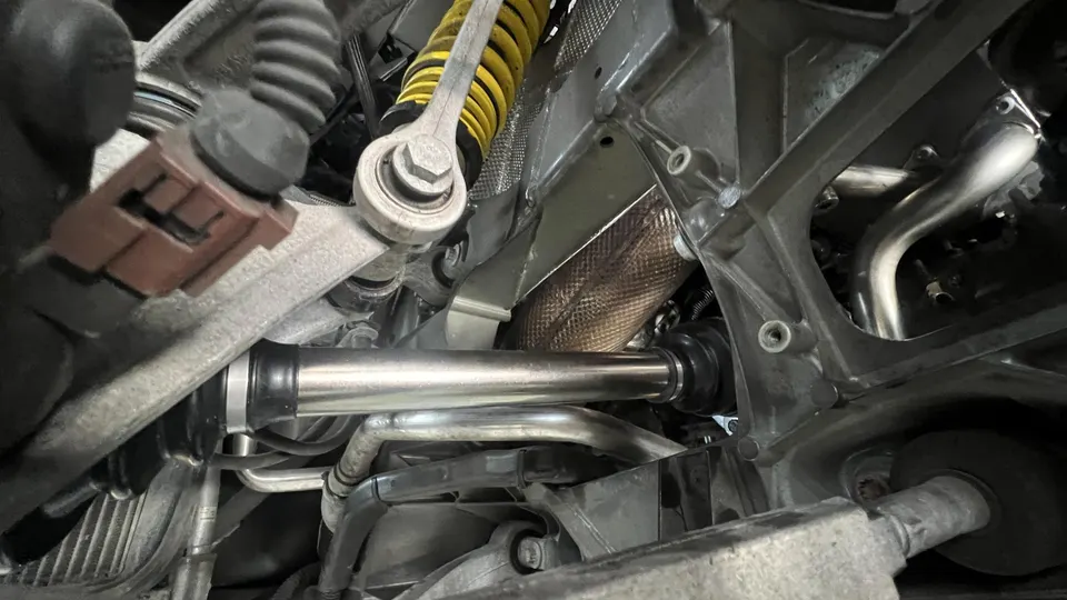 Detailed view of a car's undercarriage, highlighting the drivetrain axle, suspension coilover, and exhaust components.