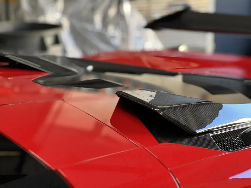 Close-up of a red supercar's carbon fiber rear wing and aerodynamic vents, showcasing exterior aero details.