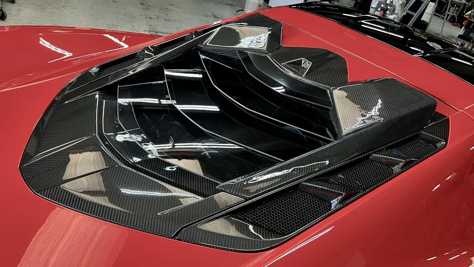 Close-up of a red supercar's carbon fiber engine cover with intricate vents and grilles.