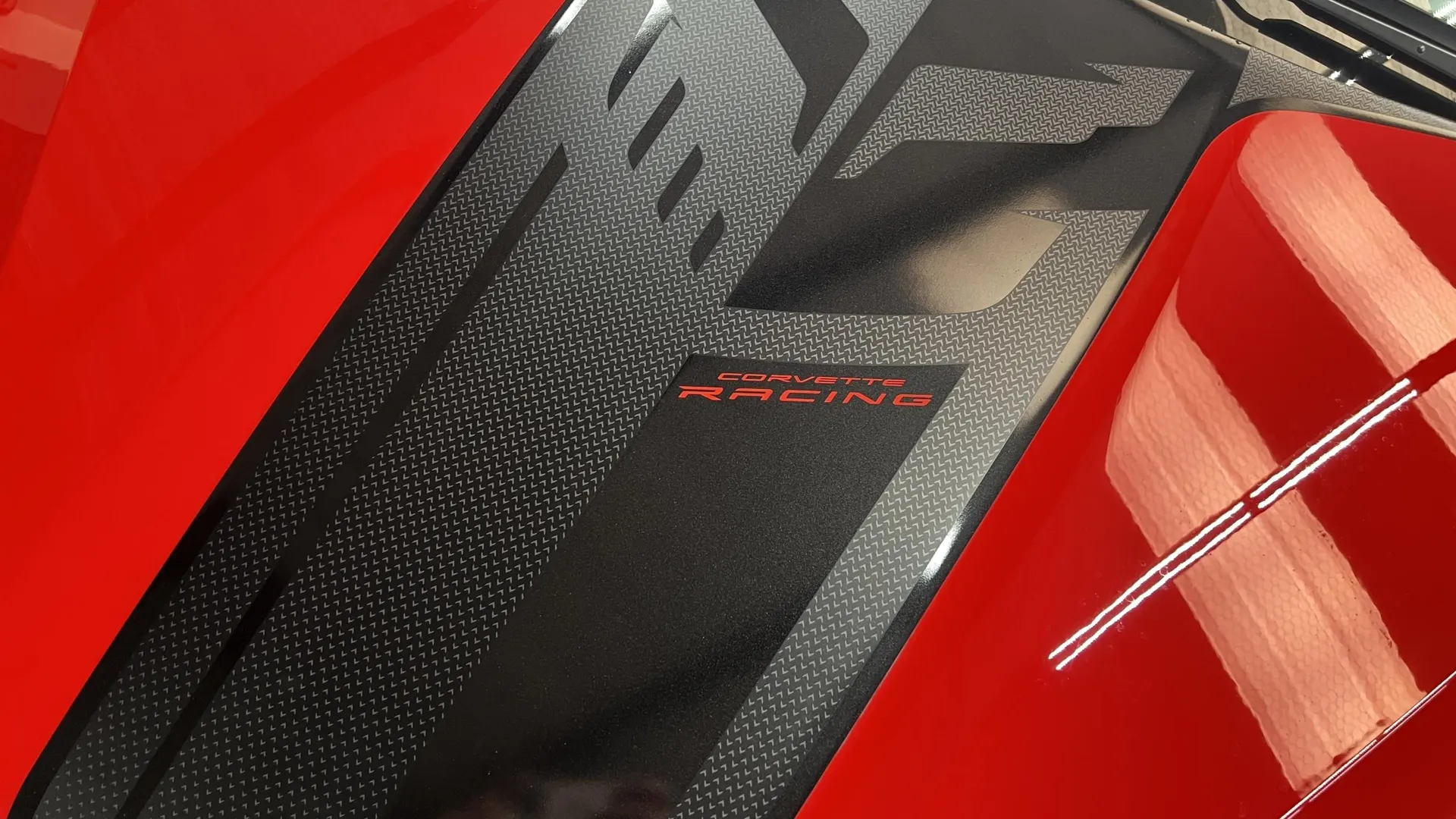 A close-up of a red Corvette's hood with a black textured graphic and a red 'Corvette Racing' decal.