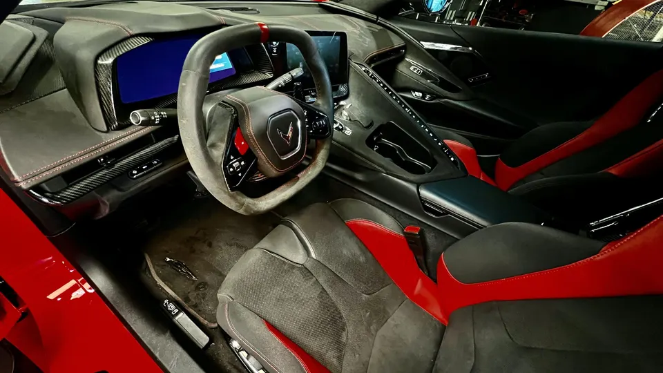 A detailed view of the red and black interior of a Chevrolet C8 Corvette, showing the steering wheel and dashboard.