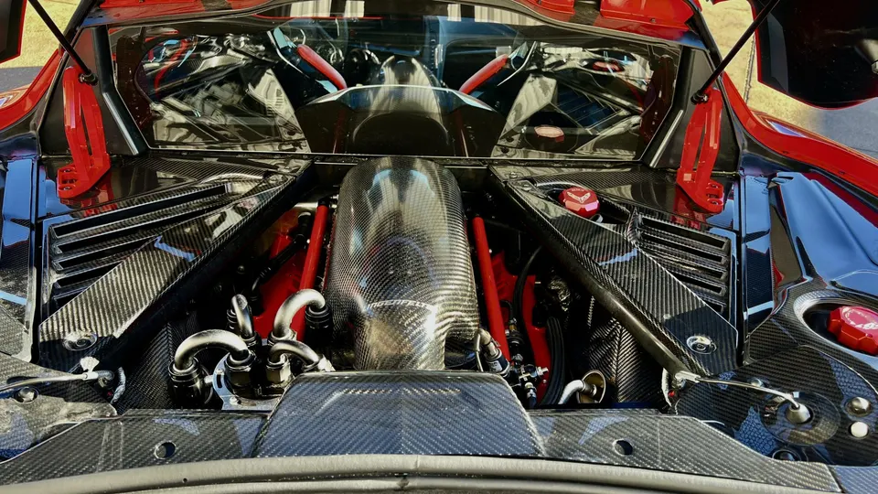 A detailed view of a C8 Corvette engine bay featuring a prominent carbon fiber intake manifold and red accents.