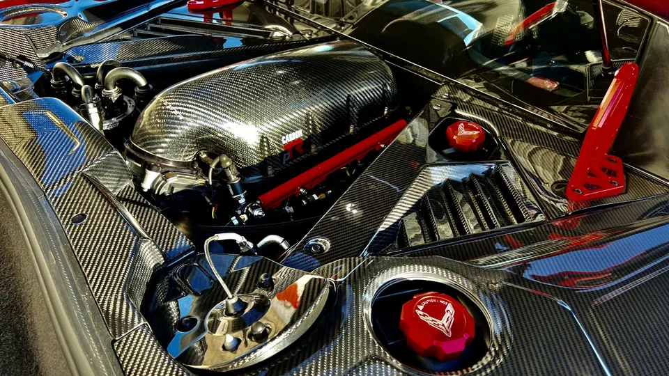 A close-up of a Corvette engine bay featuring a carbon fiber intake manifold and red accents.