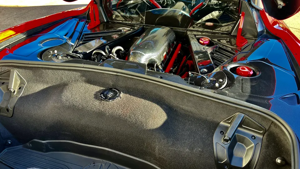 A close-up view of a supercar's engine bay featuring a prominent carbon fiber intake system and red accents.