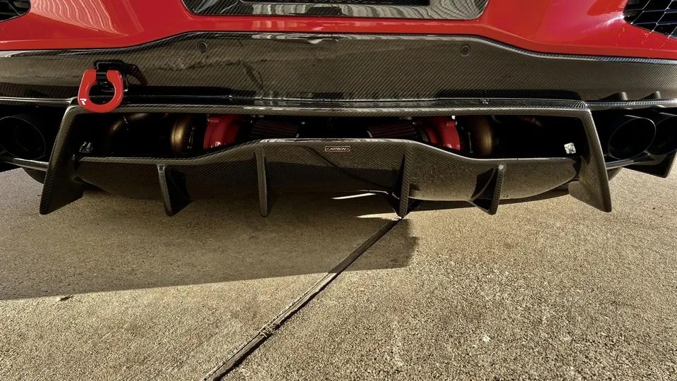 Rear view of a red performance car showcasing a Jotech carbon fiber diffuser, black exhaust tips, and a red tow hook.