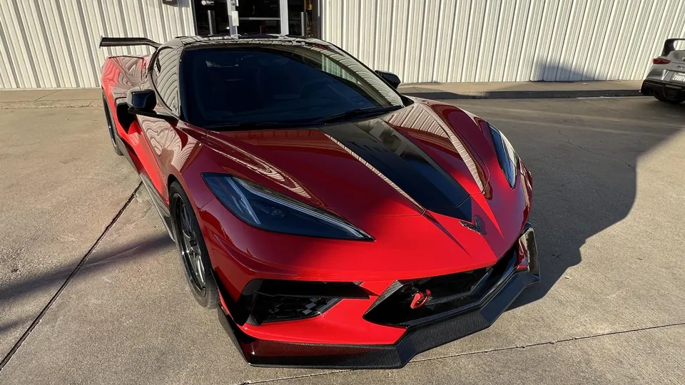 A red C8 Corvette with a black hood stripe, carbon fiber front splitter, and rear wing parked outside a building.