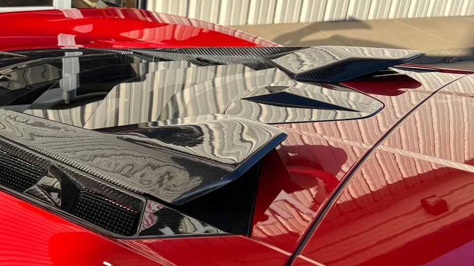 A close-up of the rear of a red supercar, showcasing a glossy carbon fiber rear wing and engine cover.