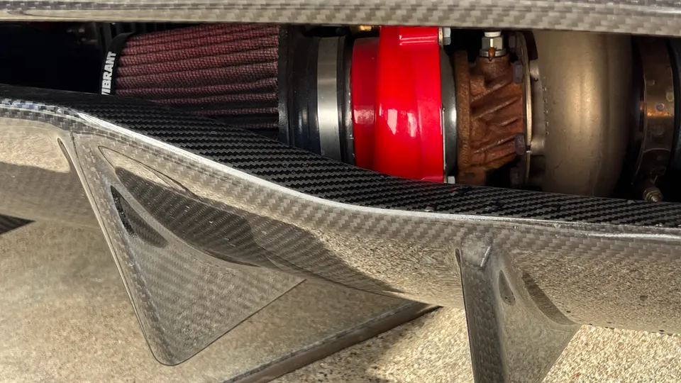 A close-up of a car's engine bay showing a red turbocharger, Vibrant air filter, and carbon fiber components.