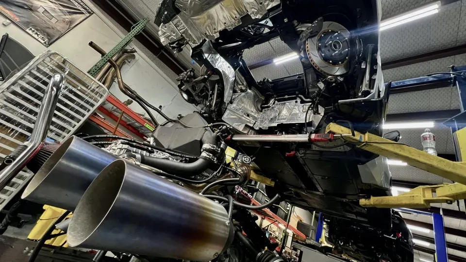 A car on a lift in a performance shop, showing a custom exhaust system and engine components during an upgrade.