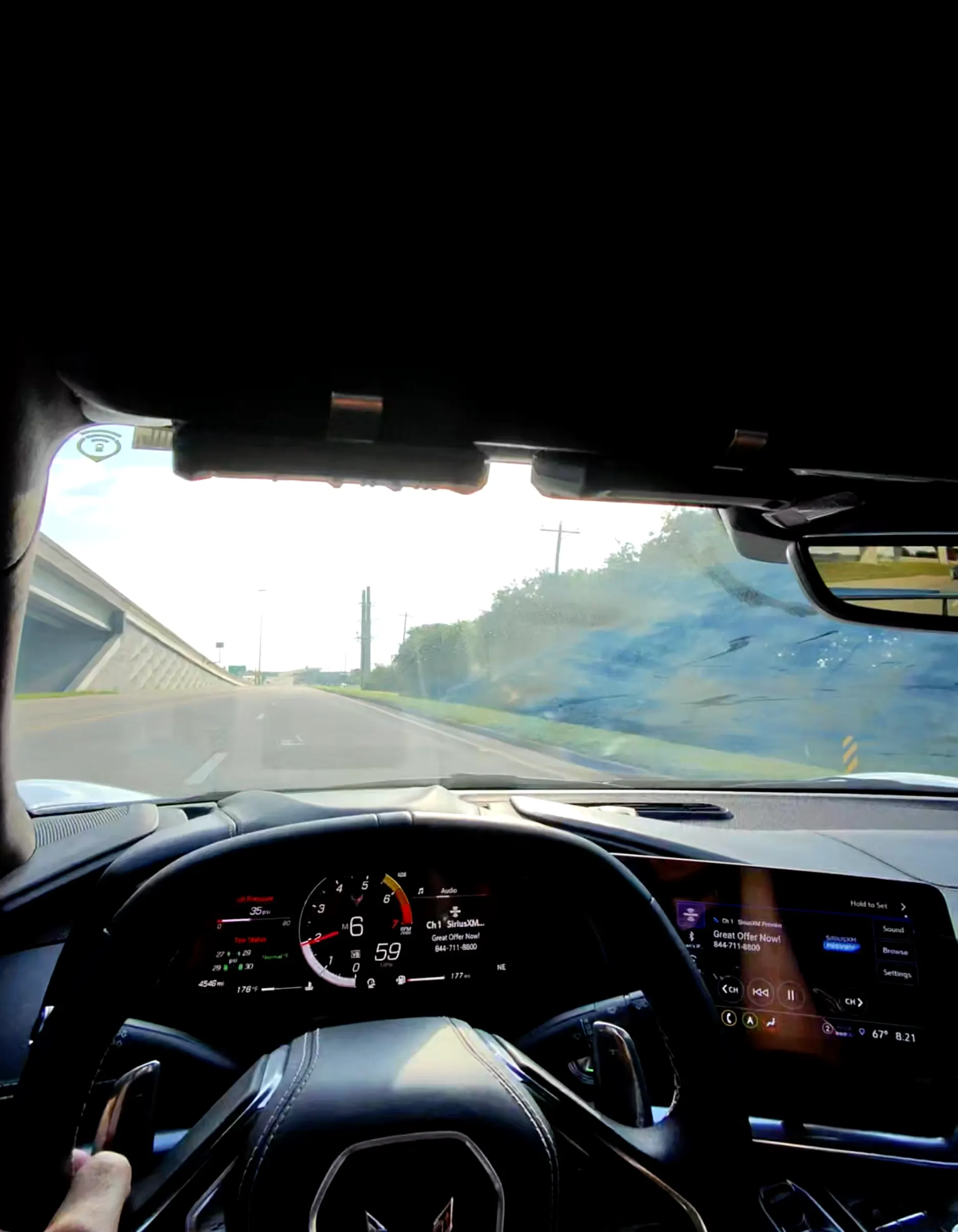 Driver's perspective of a Corvette C8 interior, showcasing the digital dashboard, steering wheel, and the road ahead.