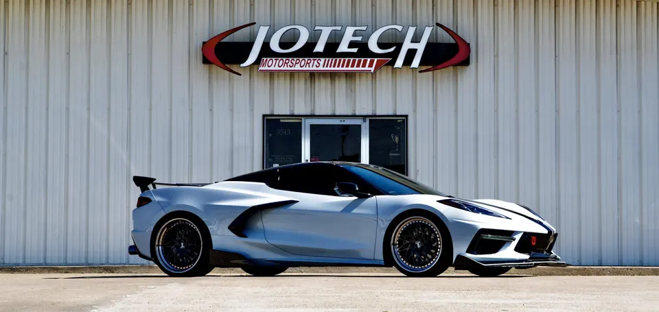 White Chevrolet Corvette C8 with aftermarket wheels, rear wing, and front splitter parked in front of Jotech Motorsports.
