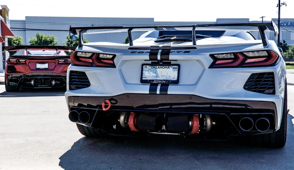 Two modified C8 Corvettes, one white and one red, showcasing their rear-mounted twin-turbo systems and large rear wings.