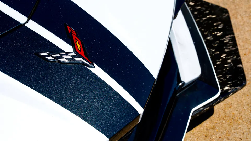Close-up of a white Corvette with a dark blue racing stripe and carbon fiber aero, featuring the iconic Corvette emblem.