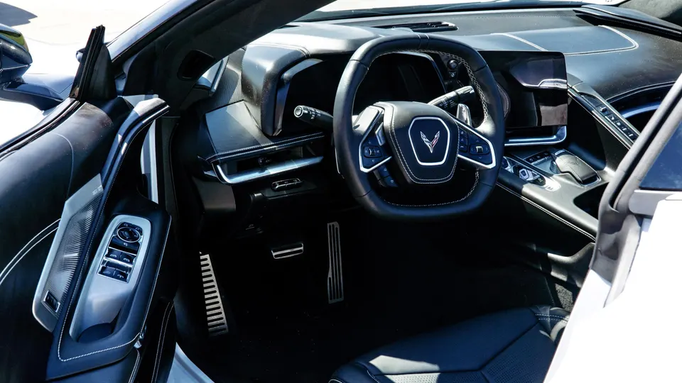 Detailed view of the black interior of a Chevrolet Corvette C8, showing the steering wheel, dashboard, and door panel.