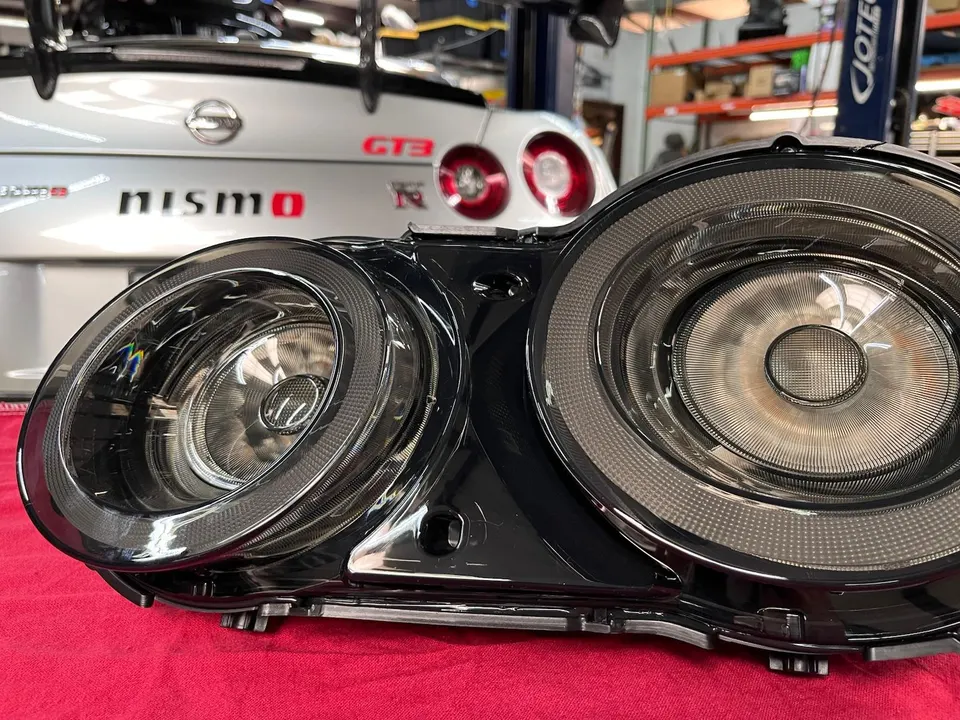 Close-up of aftermarket LED taillights for a Nissan GT-R R35, with the rear of a Nismo GT-R in a shop background.