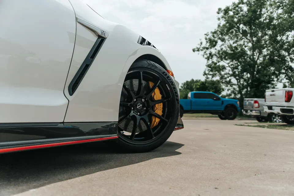 A white Nissan GT-R with black multi-spoke wheels, yellow brake calipers, and Dunlop tires.