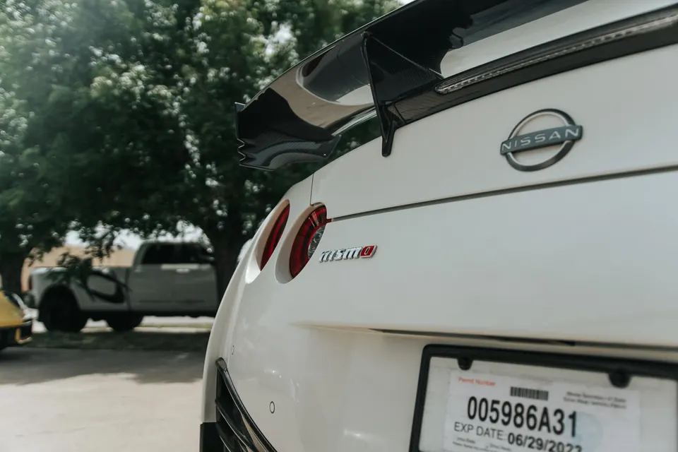 Rear view of a white Nissan GT-R Nismo with a carbon fiber rear wing and round taillights, parked outdoors.