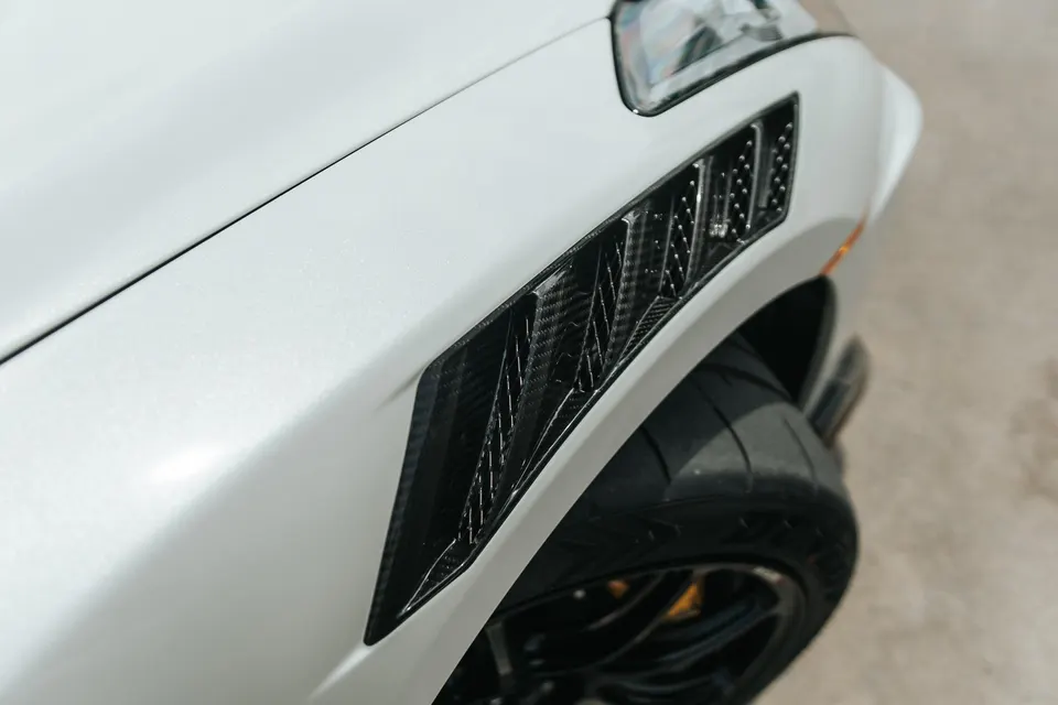 Close-up detail of a white car's fender featuring a carbon fiber vent and a performance tire.