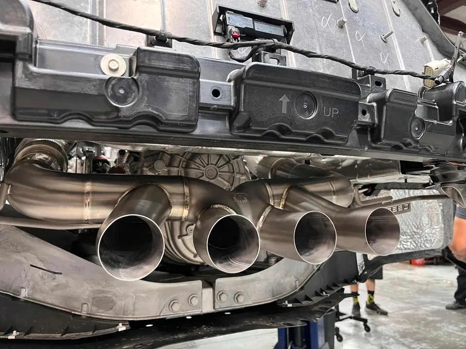 Custom stainless steel quad-tip exhaust system installed on a performance car in a shop.
