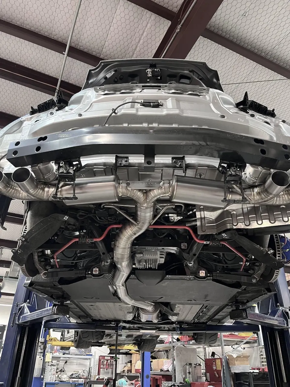 Underside view of a performance car on a lift, showcasing a custom exhaust system and red sway bars.