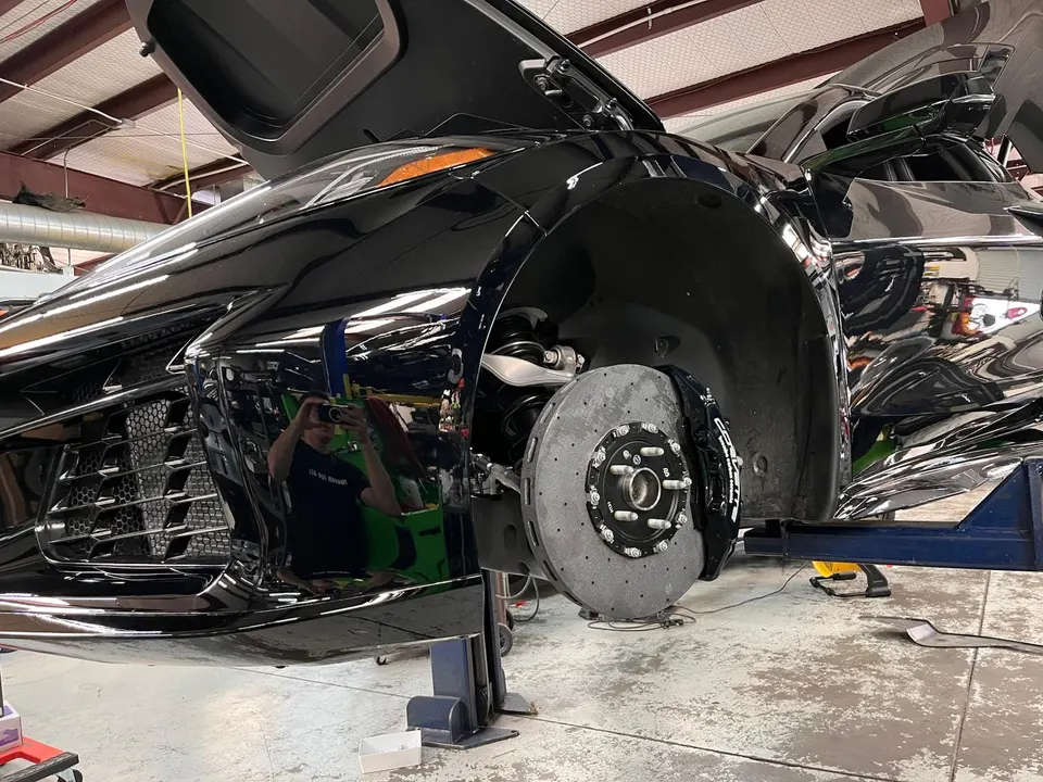 A black Lamborghini Huracan on a lift in a shop, with its carbon ceramic brakes and caliper visible.