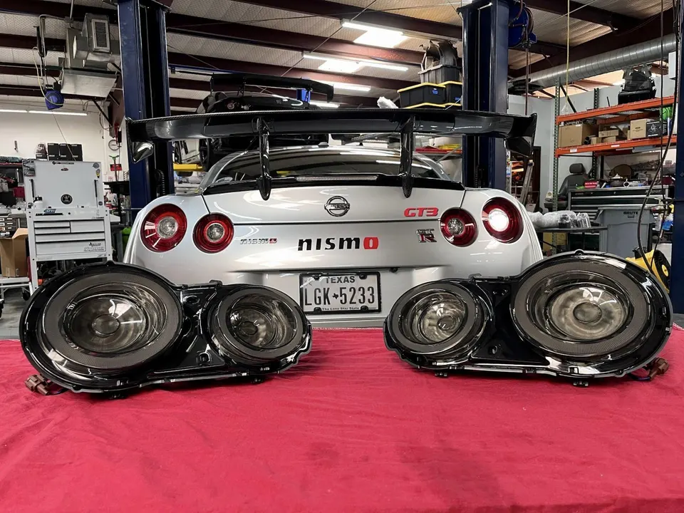 Nissan GT-R in a performance shop with aftermarket headlights displayed on a red cloth in the foreground.
