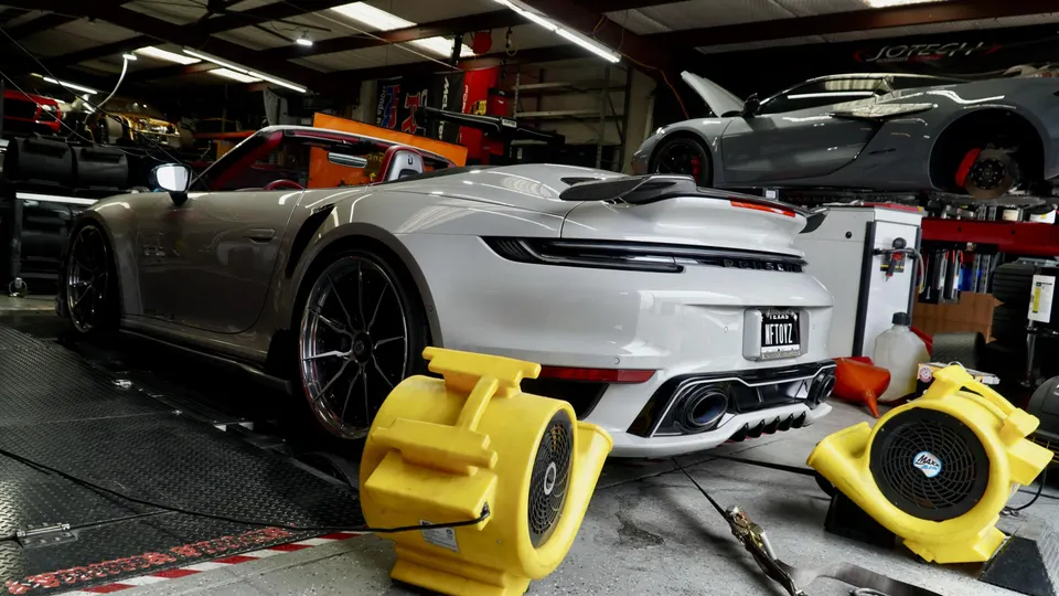 A white Porsche 911 992 convertible on a dyno at a performance tuning shop with fans blowing