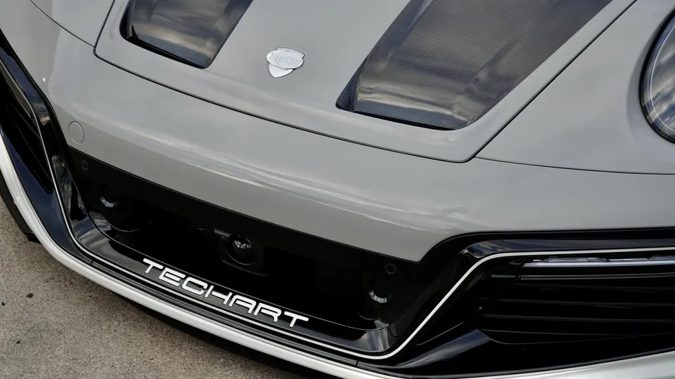 A close-up of the front of a grey TechArt Porsche, showcasing the custom bumper, hood with carbon fiber vents, and headlight.