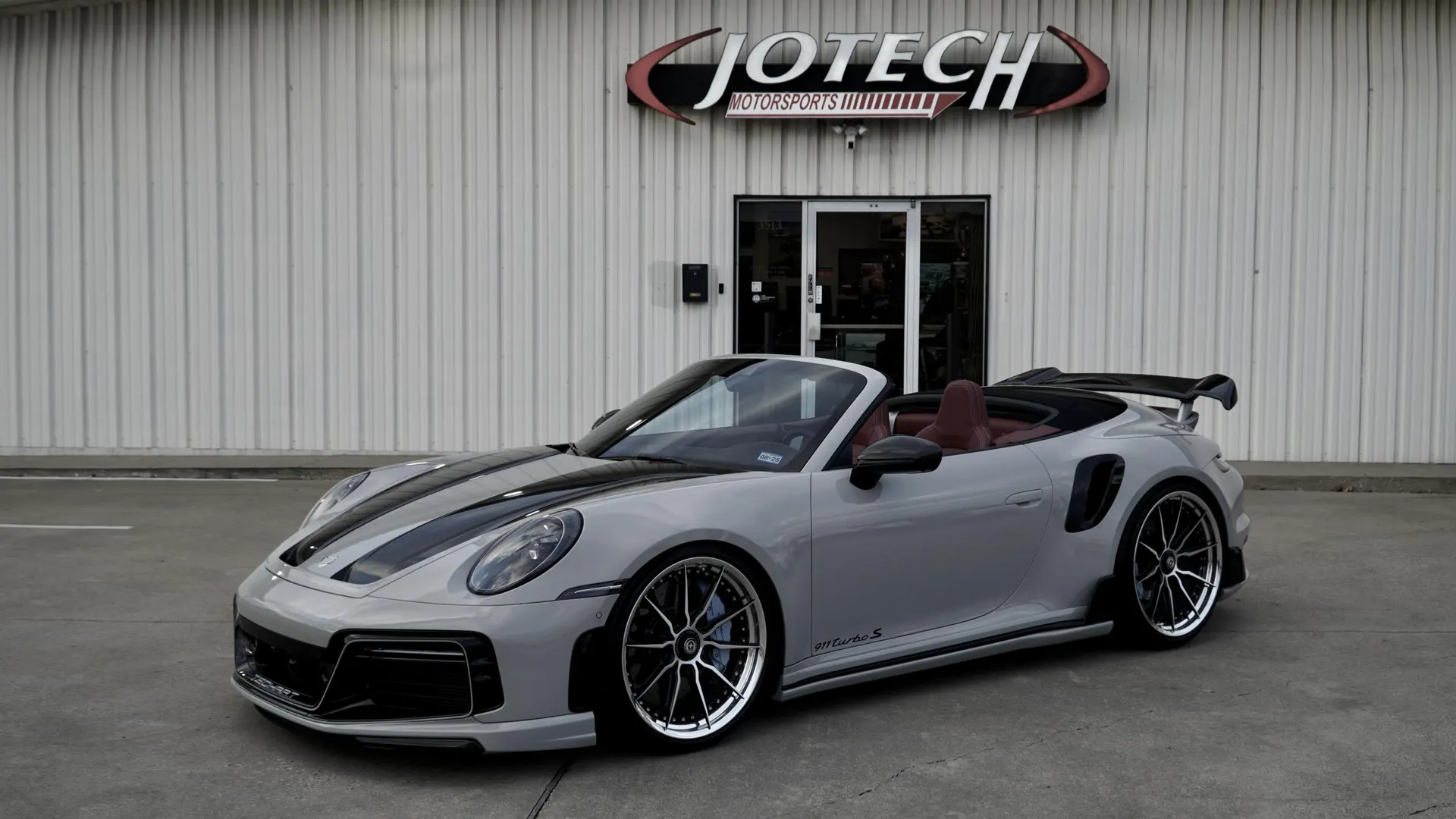 Grey Porsche 911 Turbo S convertible with aftermarket wheels and a large rear wing parked at Jotech Motorsports.
