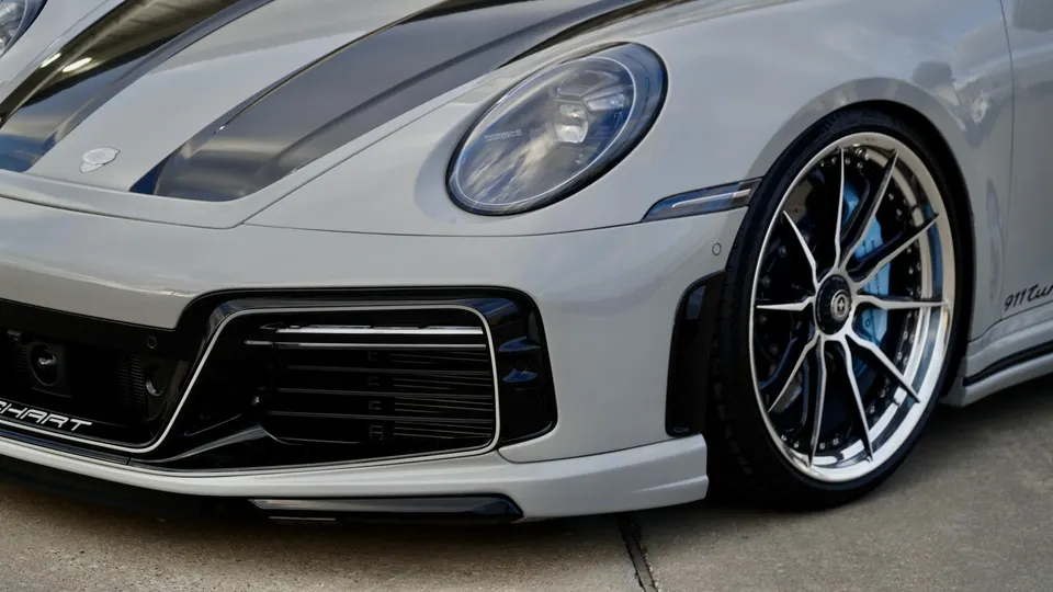 Close-up of a grey Porsche 911 Turbo S featuring custom multi-spoke wheels, blue brake calipers, and an aftermarket front bumper.