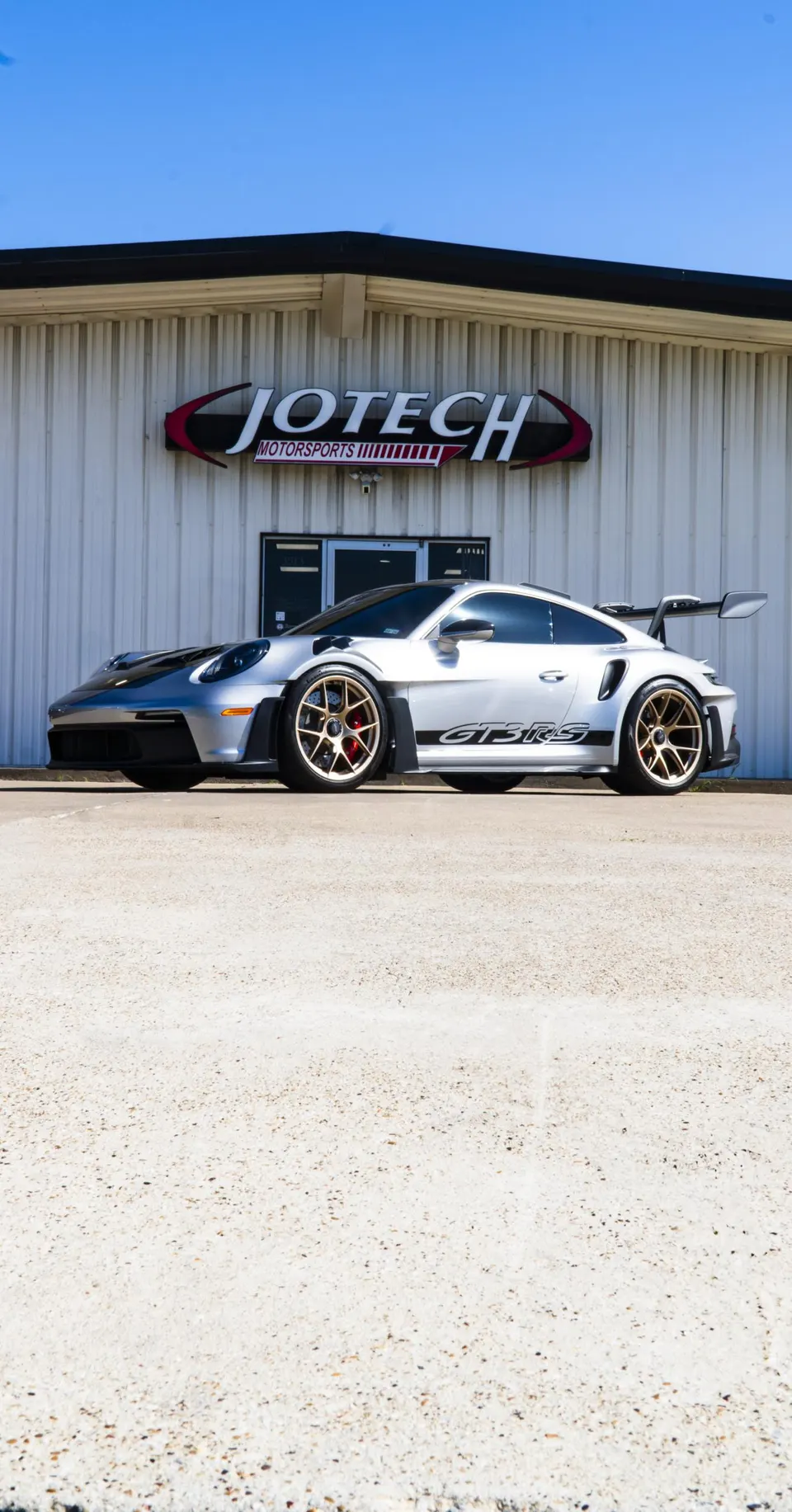 Silver Porsche GT3 RS with gold wheels parked outside Jotech Motorsports performance shop.