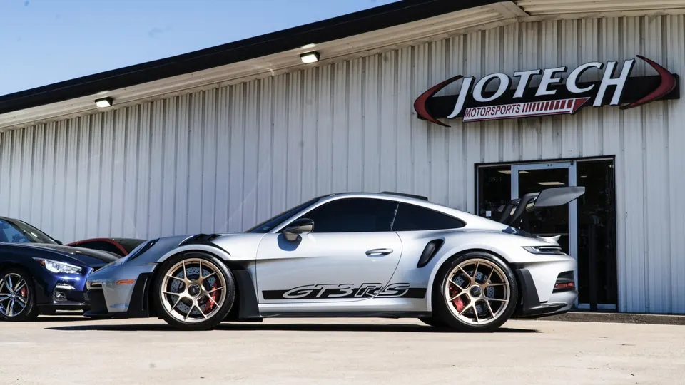 Silver Porsche GT3 RS with gold aftermarket wheels and a large rear wing parked outside Jotech Motorsports shop.