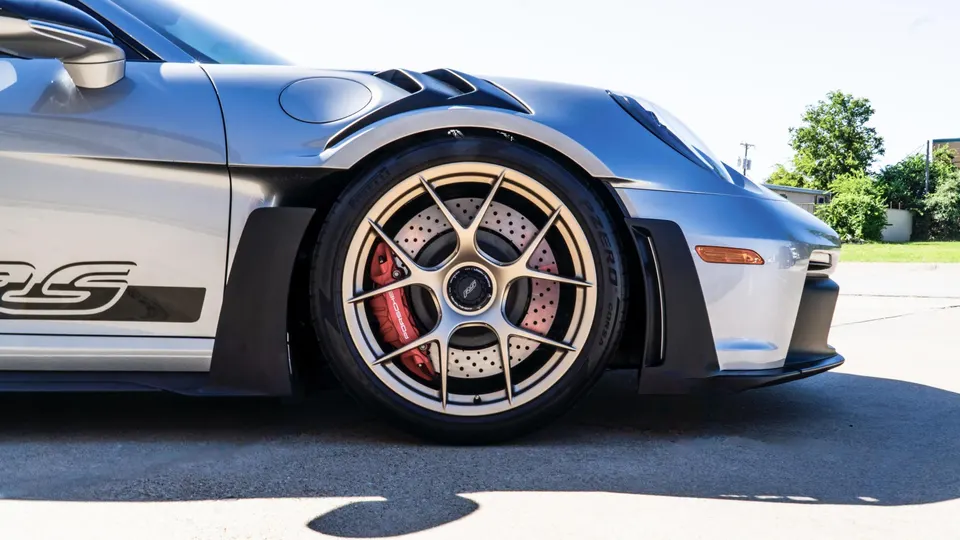 Close-up of a silver Porsche 911 GT3 RS front wheel with gold multi-spoke rims, red brake calipers, and Pirelli tires.