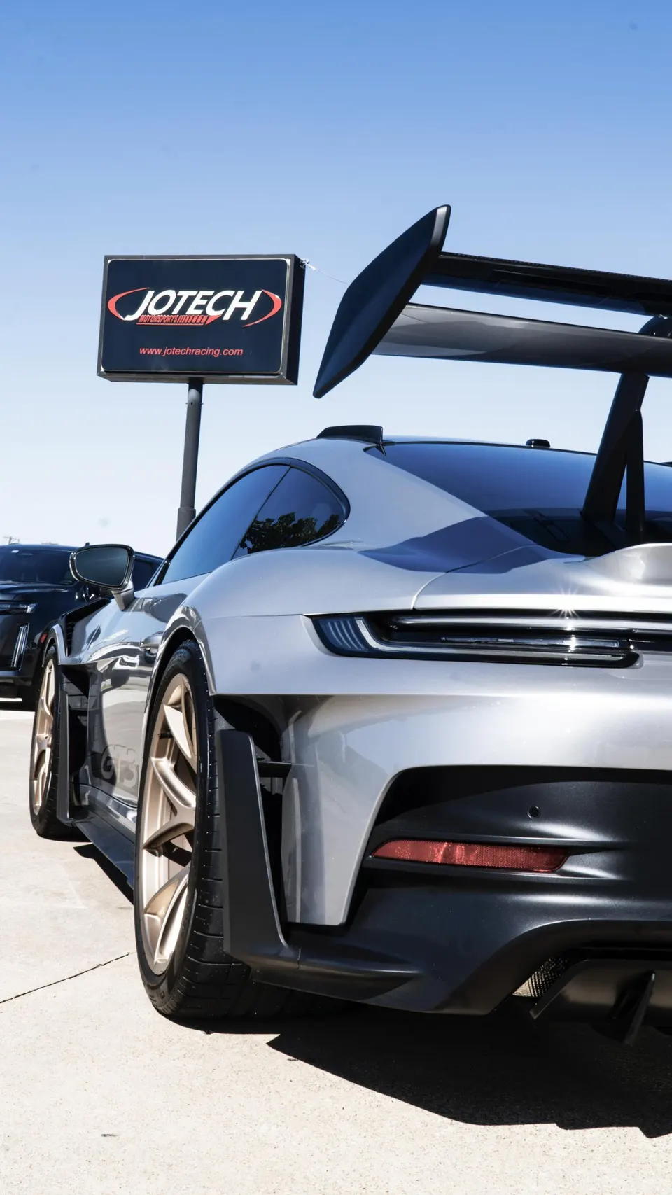 Silver Porsche 911 GT3 with a large rear wing and gold wheels parked outside Jotech Motorsports.